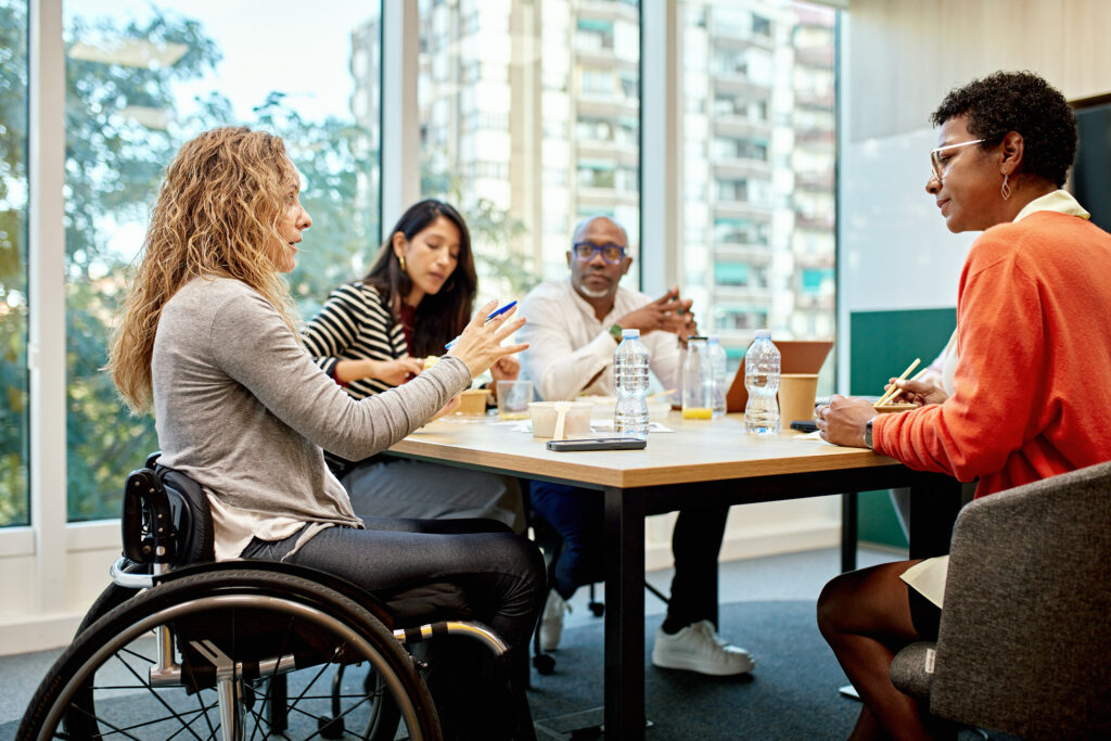 A group of adults in a conference room with large, open windows having a discussion.