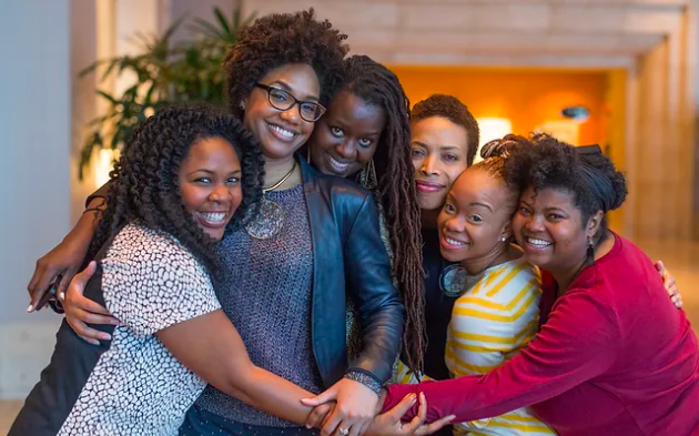 A group of women in a warmly-lit space sharing a big, group hug.