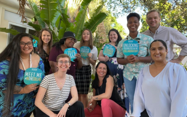 A group of ten people posing in front of tropical plants.