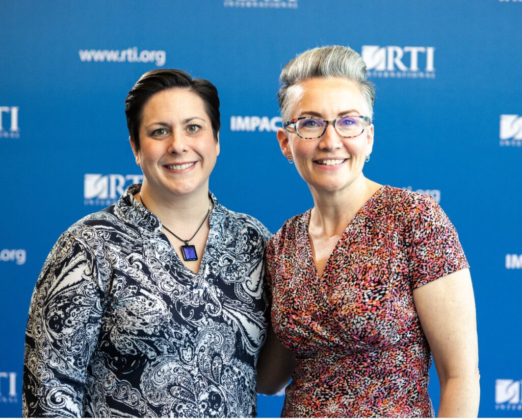Two women standing together in front of a blue backdrop.