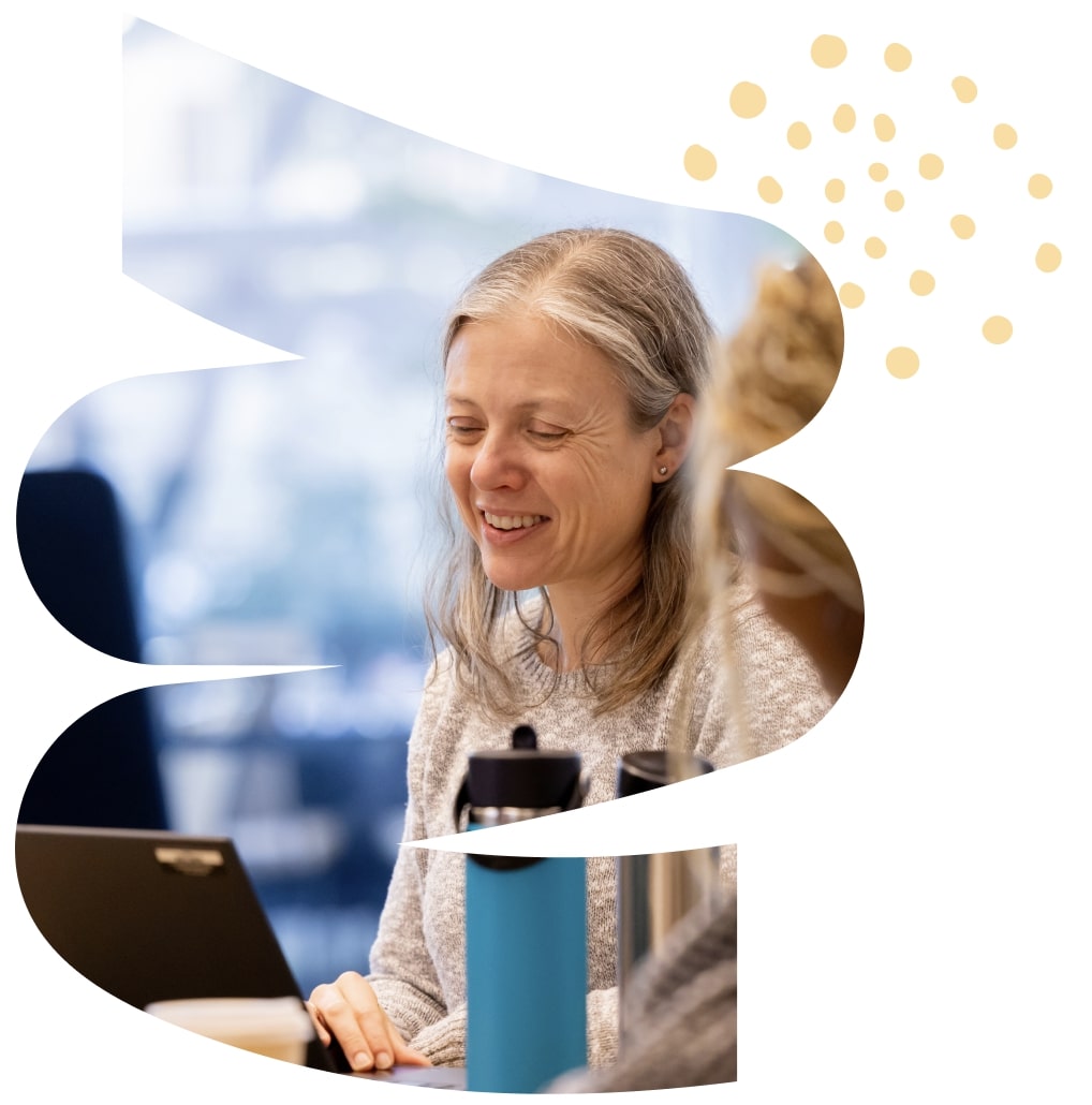 An older woman smiling and looking at a laptop with a blue water bottle in front of her.